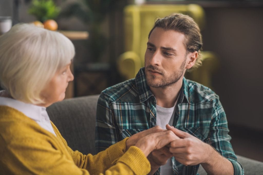 man tenderly holding his moms hands, concept of family conversation and support