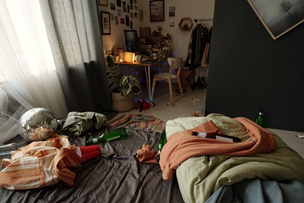 Creased clothes and empty bottles on bed, messy room concept