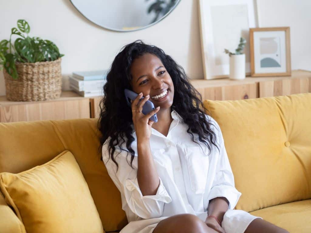 Smiling young african american woman talking on the phone sitting on the sofa