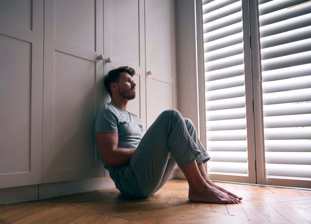 Man Suffering With Poor Mental Health Sitting On Floor At Home