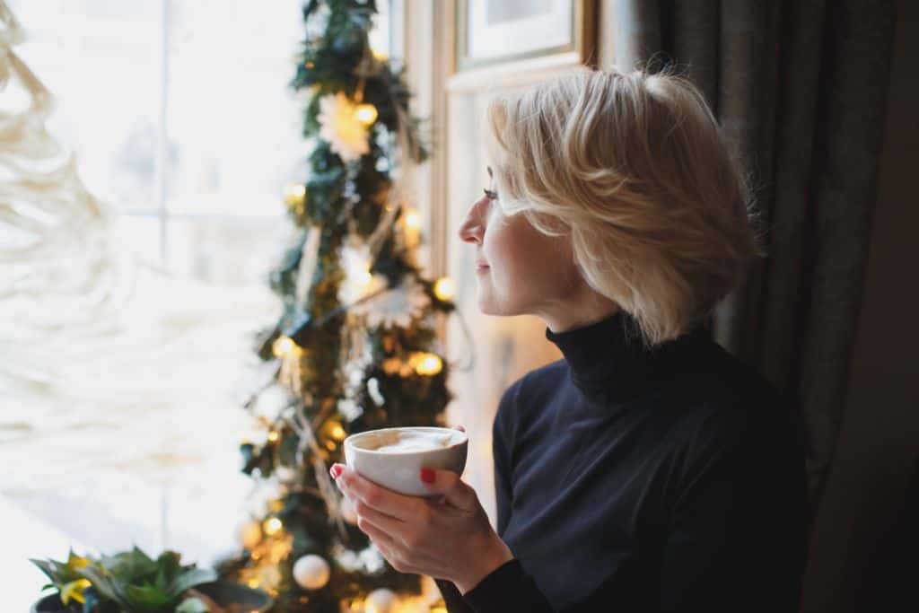 woma drinking coffee by the window near a christmas tree, concept of calm contentment during holiday