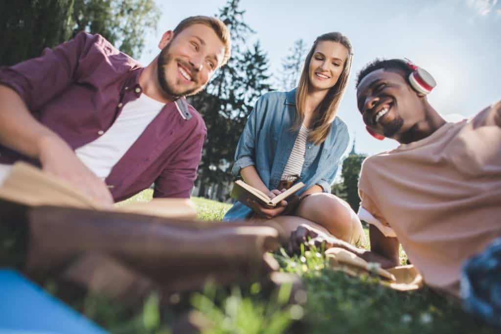 young happy students resting on grass together in park