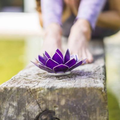 Aesthetic shot of a purple glass lotus on a tree trunk over the water. A praying woman is behind it.